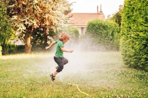 child playing in sprinkler